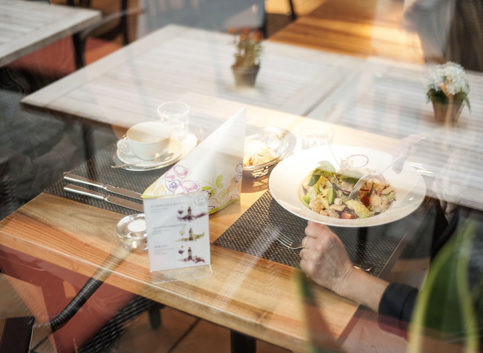 Ein Tisch im Restaurant Eugen mit einem gemischten Salatteller und einem kleinen Kaffee, betrachtet durch das Fenster. Im Bild sichtbar ist die Spieglung der Tische im Aussenbereich.