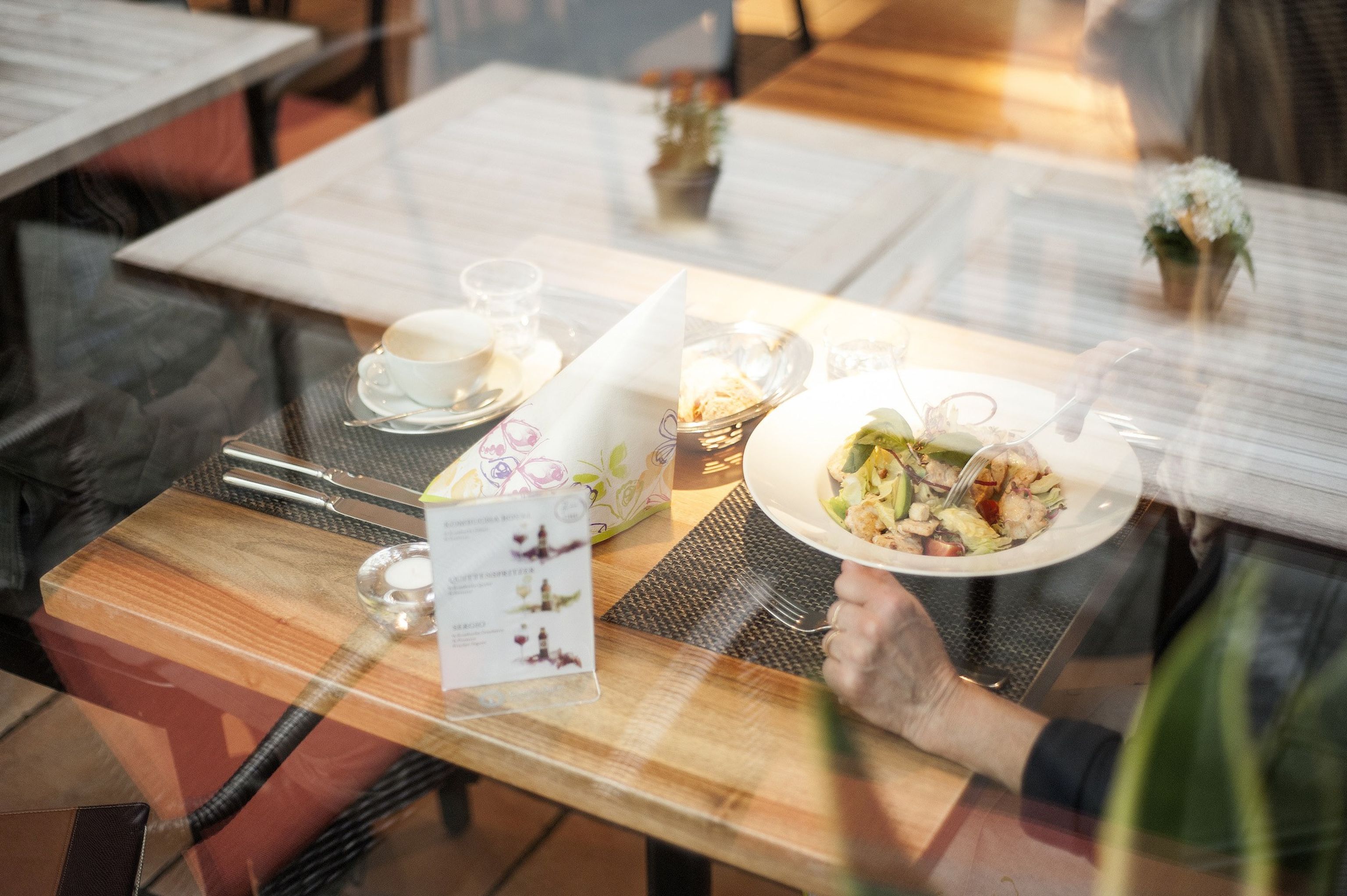 Ein Tisch im Restaurant Eugen mit einem gemischten Salatteller und einem kleinen Kaffee, betrachtet durch das Fenster. Im Bild sichtbar ist die Spieglung der Tische im Aussenbereich.